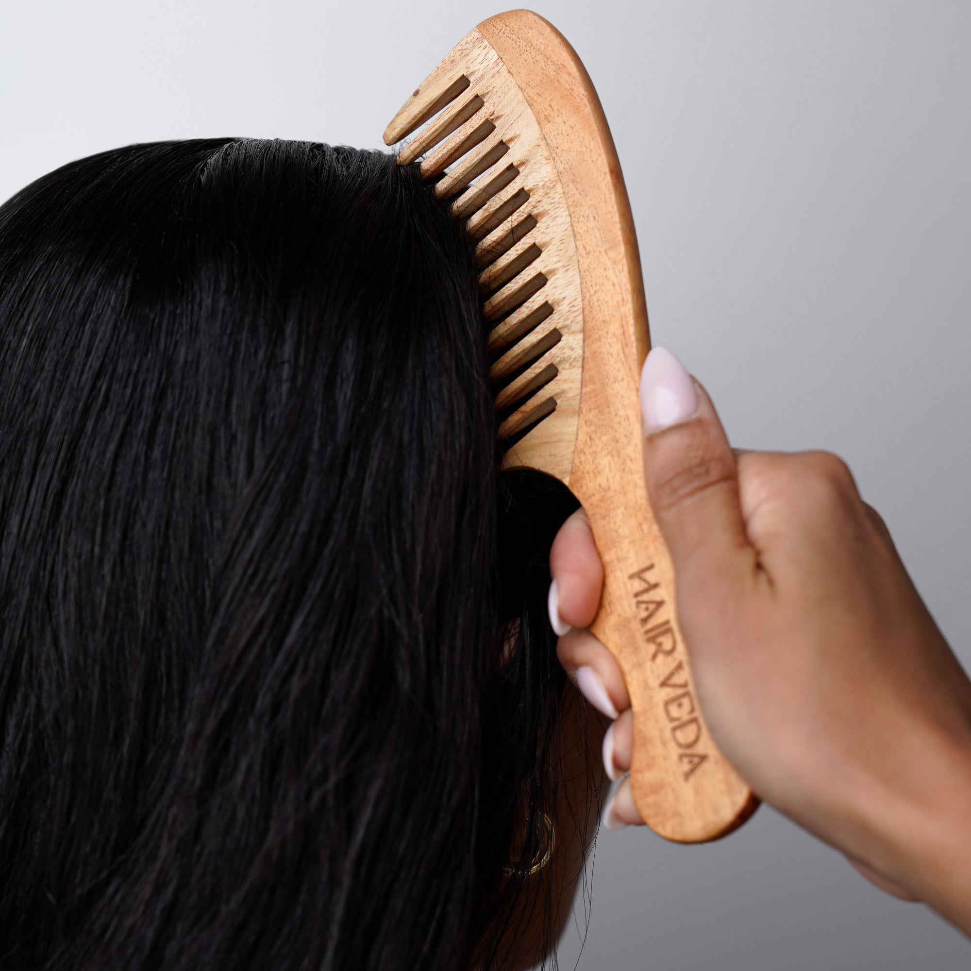 A woman combs her hair with a Neem wood hair comb, showcasing a natural and eco-friendly grooming choice.