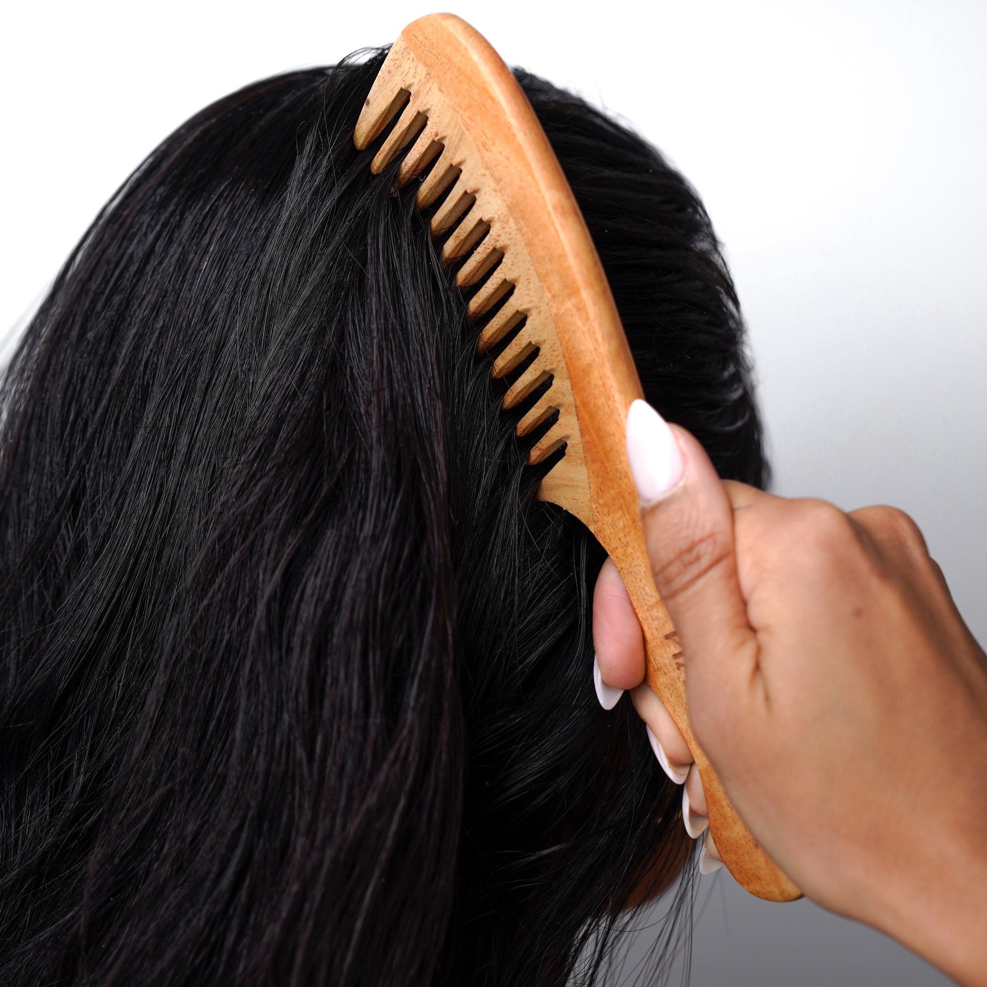 A woman combs her hair with a wooden comb, focusing on her reflection in a mirror.