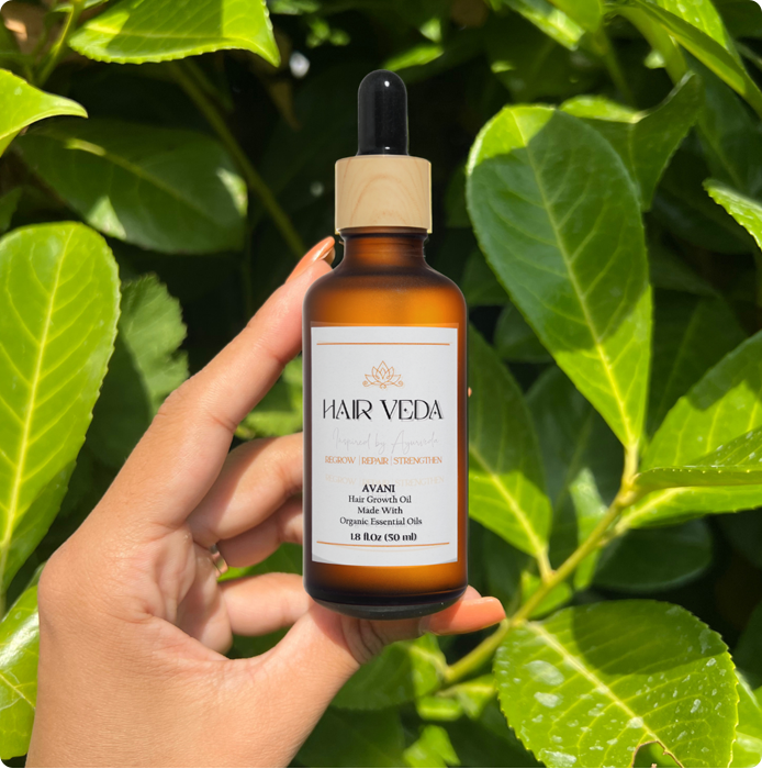 A bottle of Avani hair growth oil is displayed in front of a vibrant green leaf, emphasizing its natural ingredients.