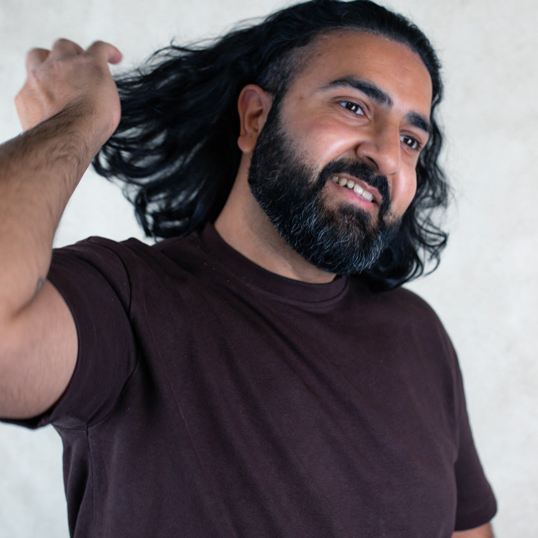 A man with long hair stands confidently, showcasing his hairstyle and casual attire.