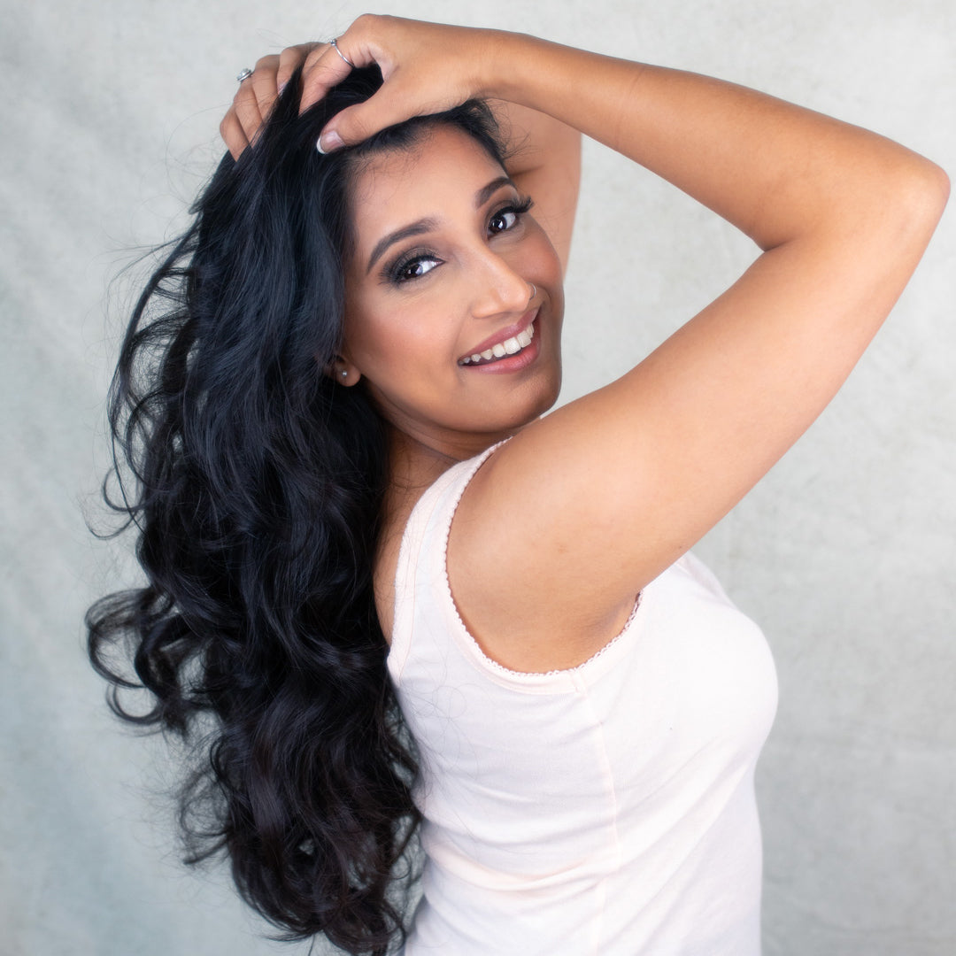 A woman with long black hair poses for a photo, showcasing Akshi brow oil in a stylish setting.