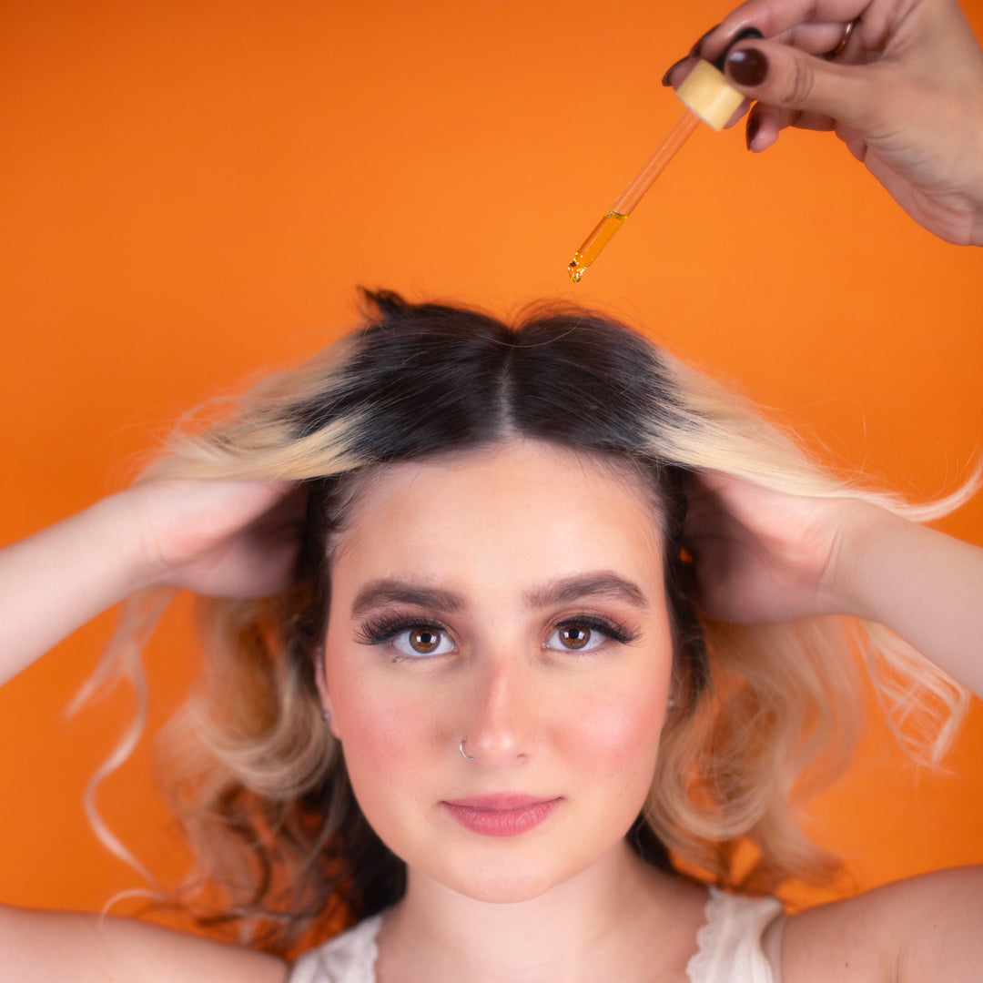 A woman with blonde hair is seated in a salon chair while a stylist works on her hair.