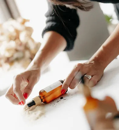 A woman places a bottle of essential oil on a wooden table, focusing on the bottle's label.