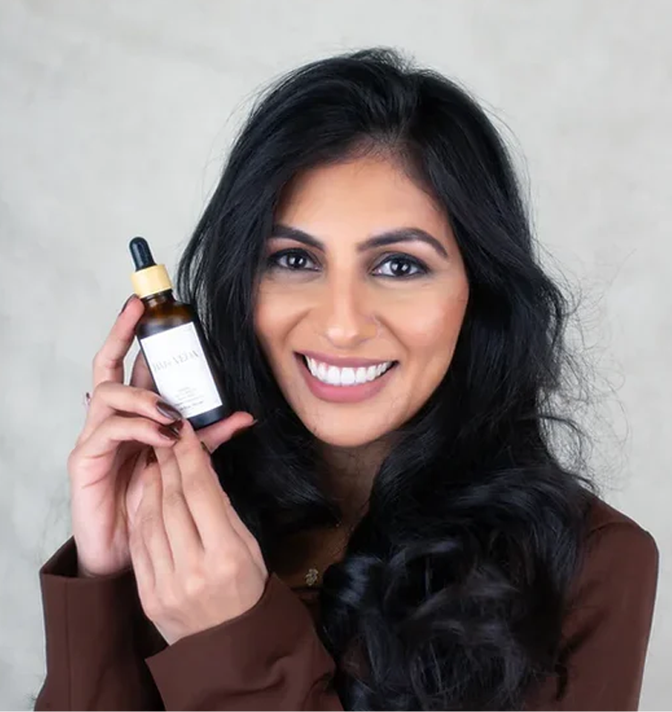 A woman with a bright smile displays a bottle of hair veda oil, emphasizing its contents.