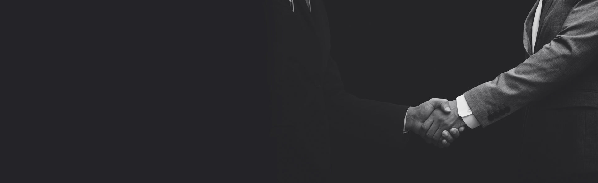 Two individuals shaking hands in a black and white photograph, symbolizing agreement or partnership.