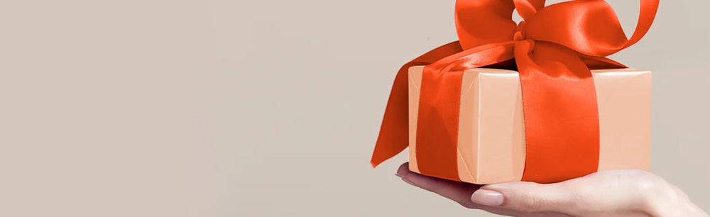 A hand holds a gift box adorned with a bright red ribbon, symbolizing celebration and generosity.